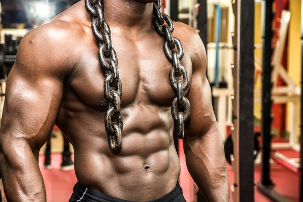 Attractive hunky black male bodybuilder doing bodybuilding pose in gym with iron chains over shoulders