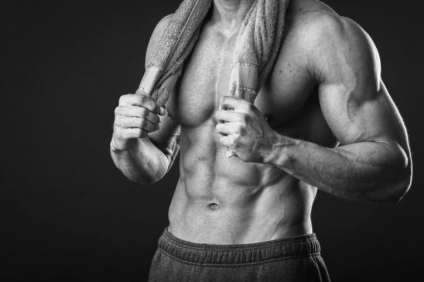Healthy muscular young man after a workout on dark background.Fitness man holding a green towel against dark background.Strong Athletic Man Fitness Model Torso showing abs. holding towel.