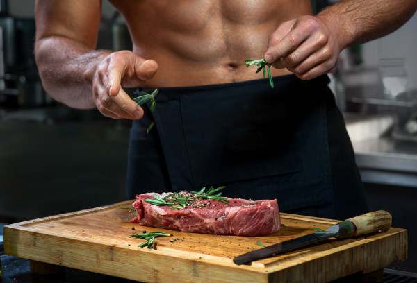 Sexy chef with naked body cooking or decorating raw meat with rosemary in the restaurant kitchen