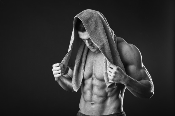 Healthy muscular young man after a workout on dark background.Fitness man holding a orange towel against dark background.Strong Athletic Man Fitness Model Torso showing abs. holding towel.