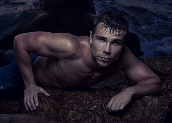 Sexy boy sits on a rock in the sea.