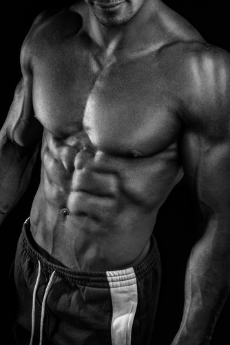 Muscular and fit young bodybuilder fitness male model posing over black background. Studio shot on black background.