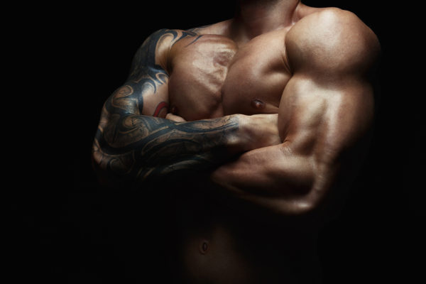 Athletic man's torso. Unrecognizable male fitness model show naked muscular body. Strong hands, chest and shoulder muscles and biceps. Studio shot on black background, low key. Bodybuilding concept